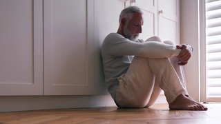 Symbolbild für Altersdepression. Ein Mann sitzt auf dem Boden und wirkt dabei sehr niedergeschlagen. Psychiaterin Katharina Domschke spricht in SWR1 Leute über Depression und wie sie behandelt wird.