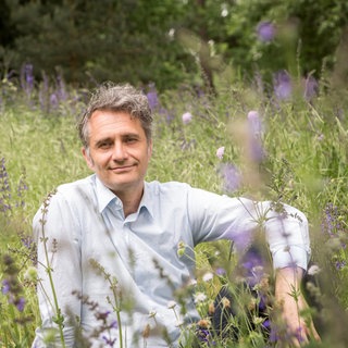 Andreas Weber, Biologe und Philosoph, sitzt in einer blühenden Wiese.