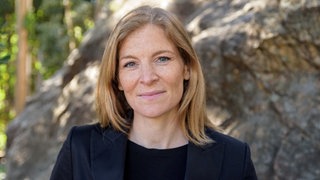 Astrid Langer, USA-Korrespondentin NZZ, lächelt vor einem Felsen stehend in die Kamera.