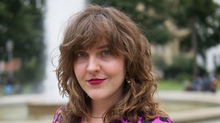 Autorin und Feministin Cleo Libro steht vor einem Springbrunnen und schaut freundlich in die Kamera. Feministin und Podcasterin Cleo Libro schreibt über geheime Fantasien, aufregende Flirts und missglückte One-Night-Stands. Seit 2018 spricht und schreibt sie unter ihrem Pseudonym über sexuelle Selbstbestimmung, Feminismen und Lust und Frust.