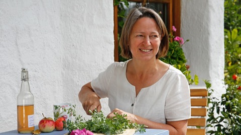Ernährungswissenschaftlerin Karin Buchart sitzt im Garten und schneidet Kräuter. Sie erklärt in SWR1 Leute, welche Heilkräuter und Heilpflanze welche Wirkung haben und wie Naturheilkunde uns heilen kann.