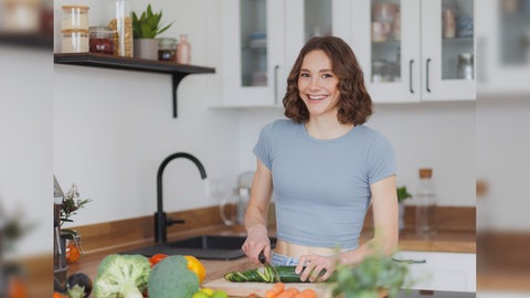 Foodbloggerin fitgreenmind Maya Leinenbach schneidet eine Gurke und lächelt in die Kamera. Sie spricht in SWR1 Leute über ihre Ernährung, vegane Rezepte und ihre Social Media-Accounts.