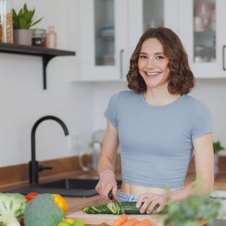 Foodbloggerin fitgreenmind Maya Leinenbach schneidet eine Gurke und lächelt in die Kamera. Sie spricht in SWR1 Leute über ihre Ernährung, vegane Rezepte und ihre Social Media-Accounts.