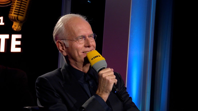 Entertainer Harald Schmidt hält ein Mikrofon vor den Mund und streckt den Arm aus. Anlass ist eine Jubiläumssendung zum 40 Jahre SWR1 Leute.