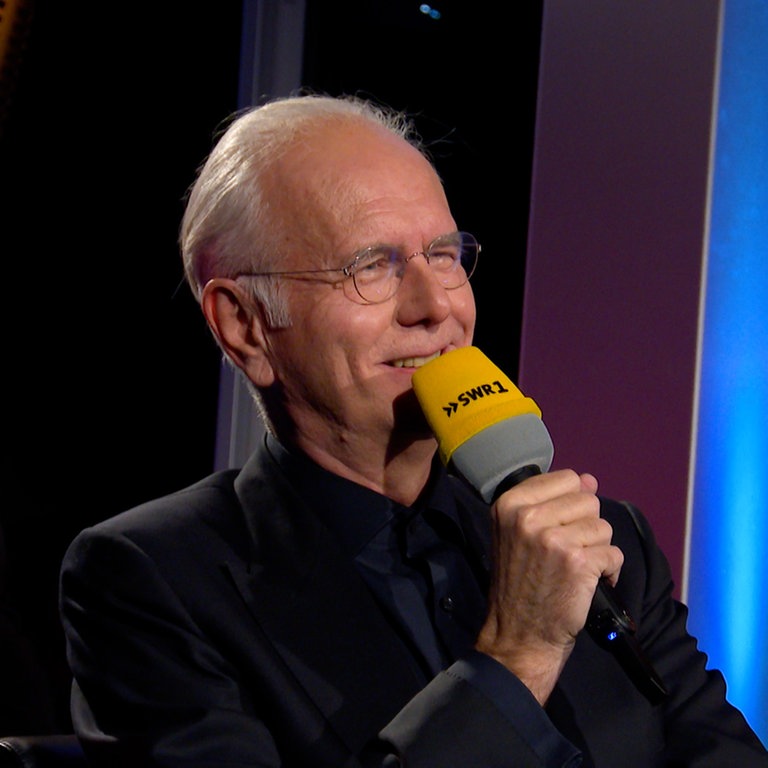 Entertainer Harald Schmidt hält ein Mikrofon vor den Mund und streckt den Arm aus. Anlass ist eine Jubiläumssendung zum 40 Jahre SWR1 Leute.