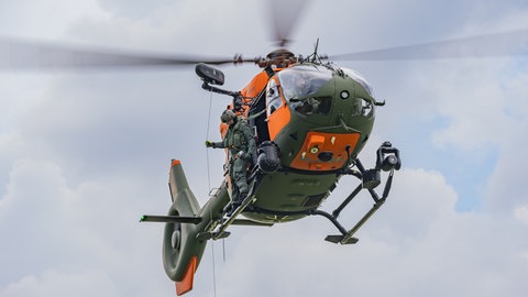 Dennis Prosser, Lufretter bei der Bundeswehr steht auf dem fliegenden Hubschrauber. Er ist zu Gast in SWR1 Leute. | Bundeswehr-Luftretter Dennis Prosser hat Menschen bei der Ahrtal-Flutkatastrophe gerettet