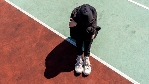 Ein Mädchen sitzt auf dem Boden und vergräbt ihr Gesicht in den Händen. Kinder- und Jugendcoach Angelika Fuchs gibt Eltern und Kindern Tipps, wie man Mobbing bekämpfen und am besten damit umgehen kann.