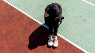 Ein Mädchen sitzt auf dem Boden und vergräbt ihr Gesicht in den Händen. Kinder- und Jugendcoach Angelika Fuchs gibt Eltern und Kindern Tipps, wie man Mobbing bekämpfen und am besten damit umgehen kann.