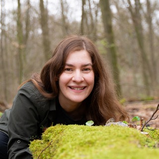 Naturfotografin Farina Graßmann liegt im Wald auf einem bemoosten Stein. Sie erforscht True Crime in der Natur bei Tieren und Pflanzen.