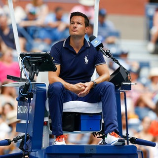 Nico Helwerth, deutscher Grand Slam-Tennis-Schiedsrichter, sitzt auf einem Schiedsrichter-Stuhl am Tennis Court. Als Schiedsrichter ist Nico Helwerth aus deutscher Sicht gesetzt bei den großen Tennis-Turnieren dieser Welt. In SWR1 Leute erzählt er, wie nervenstark ein Schiedsrichter bei den großen Tennis-Turnieren wie der US Open, French Open oder Australian Open sein muss.
