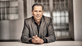 Škoda-Chef Klaus Zellmer sitzt mit aufgestützen Ellenbogen und in einander gelegten Händen an einem Tisch. In SWR1 Leute spricht er über den Weg in die Mobilität der Zukunft.