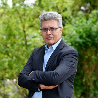 Traumaforscher Jan Ilhan Kizilhan schaut mit verschränkten Armen in die Kamera. Wir sprechen mit ihm über Menschen, die Krieg, Terror und Gewalt erlebt haben und deshalb an einem Trauma leiden.