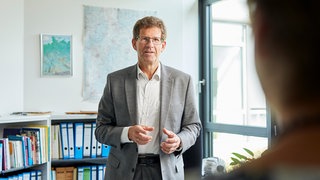 Klima-Experte Volker Kienzlen steht in einem Büro, im Hintergrund sind Aktenordner. Wie kann kommunaler Klimaschutz aussehen? Welche Möglichkeiten der Energieeinsparung habe ich? Was kosten konkrete Klimaschutzprojekte die Gemeinden? Fragen an Dr. Volker Kienzlen, den Geschäftsführer der Klimaschutz- und Energieagentur BW, in SWR1 Leute.