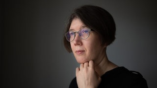 Inna Hartwich hält ihre Hand ans Kinn und schaut seitlich an der Kamera vorbei.