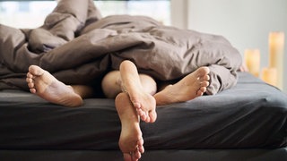 Eine Frau und ein Mann liegen eng umschlungen in einem Bett. (gestellte Szene)