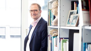 Lutz Jäncke, Neurowissenschaftler, steht seitlich und schmunzelt in die Kamera.