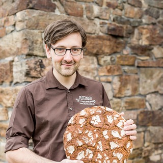 Lutz Geißler, Der Brotpapst, hält einen Laib Brot in den Händen. Lutz Geißler gilt als Deutschlands Brotpapst. "Jeder kann Brot backen", sagt er, und beweist das mit über 20 Büchern und 2.000 Brotrezepten. In SWR1 Leute erzählt er von der Faszination Brot.