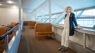 Kunsthistorikerin Dr. Claudia Emmert lehnt sich an und schaut in die Kamera.