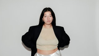 Yasmine M’Barek, Journalistin und Autorin, hat ihre Arme hinter dem Rücken und schaut in die Kamera.