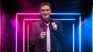 Kabarettist Mathias Richling lächelt vor einer leuchtenden Wand.