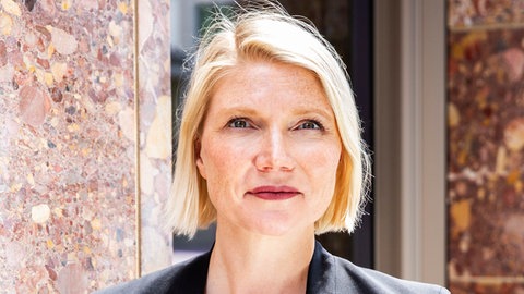 Cathryn Clüver Ashbrook, deutsch-US-amerikanische Politologin, schaut direkt in die Kamera.  Befinden sich die USA mitten im Umbau zur Autokratie, wird die Demokratie ausgehölt? Greifen diese Muster auch in Europa? Politikwissenschaftlerin Catryn Clüver Ashbrook analyisiert in ihrem Buch "Der amerikanische Weckruf" die Politik von US-Präsident Donald Trump. Sie ist zu Gast in SWR1 Leute.