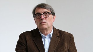 Germanist Christoph Bartmann hält sich mit einer Hand am Geländer fest und steckt die andere Hand in die Hosentasche.  Kann der Kulturkampf, den Donald Trump in den USA angezettelt hat, ein Vorbild für deutsche Rechtspopulisten sein? Der Germanist Christoph Bartmann beobachtet das sehr genau. In SWR1 Leute sprechen wir mit ihm darüber, wie Rechtspopulisten versuchen, völkische Ideologien über den Einfluss auf Kulturinstitutionen zu etablieren.