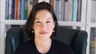 Journalistin Ceyda Nurtsch sitzt vor einem Bücherregal und schaut freundlich in die Kamera.