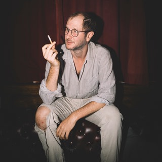 Musiker Marco Wanda hält eine Zigarette in der Hand und schaut von der Kamera weg. 