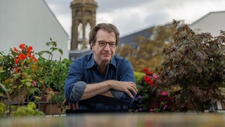 Andreas Hoffmann, Journalist, sitzt mit verschränkten Armen an einem Gartentisch.
