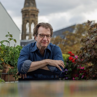 Andreas Hoffmann, Journalist, sitzt mit verschränkten Armen an einem Gartentisch.