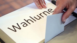 In einem Wahllokal wird ein Stimmzettel in eine Wahlurne geworfen. Mit dem Kommunikationswissenschaftler Prof. Frank Brettschneider schauen wir in SWR1 Leute auf Gewinner und Verlierer der Landtagswahl Baden-Württemberg, auf den neuen Ministerpräsidenten und welche Koalitionen realistisch sind.