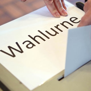 In einem Wahllokal wird ein Stimmzettel in eine Wahlurne geworfen. Mit dem Kommunikationswissenschaftler Prof. Frank Brettschneider schauen wir in SWR1 Leute auf Gewinner und Verlierer der Landtagswahl Baden-Württemberg, auf den neuen Ministerpräsidenten und welche Koalitionen realistisch sind.