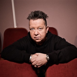 Musiker Sebastian Krumbiegel lehnt mit den Armen auf den Rückenlehnen der vorderen Sitzreihe.