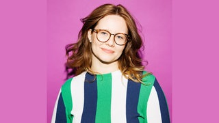 Leonie Schöler, Historikerin, steht vor einen pinken Hintergrund