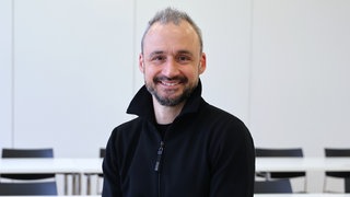 Gesundheitsökonom Jan-Marc Hodek lacht in die Kamera. In SWR1 Leute spricht er über die GKV-Reform.