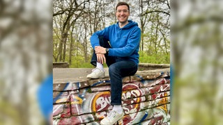 Bestsellerautor David Nelles sitzt auf einer mit Graffiti besprühten Mauer. | Wie wär's mit konkreten Lösungen? David Nelles macht Vorschläge beim Klima und anderen Streitthemen