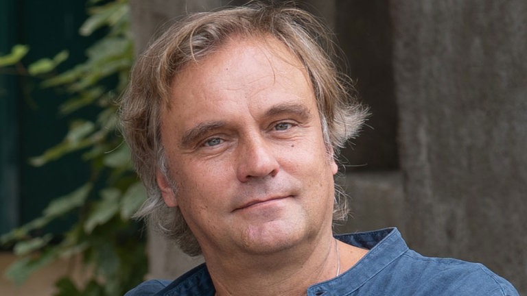 Autor Stefan Maiwald schaut freundlich in die Kamera. Stefan Maiwald schreibt historische Romane, humorvolle Sachbücher und kulinarische Reiseführer. In SWR1 Leute nimmt er uns mit in seine Wahlheimat Italien und erklärt, warum er das "bella vita" und Italien so sehr liebt. In seinem Buch "Espresso unter Sternen" zieht es ihn nach Triest, um tief in die italienische Seele zu blicken. Hier testet er, wie wir das eigene Leben ein wenig besser und glücklicher gestalten können.