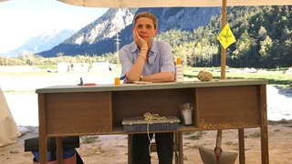 Felicitas Hoppe, Reiseschriftstellerin, sitzt an einem Holzschreibtisch unter einer Zeltplane in freier Natur.