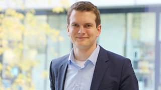 Dr. Titus Brinker, KI-Experte, lacht in die Kamera. Er verrät, wie Künstliche Intelligenz die Medizin verändert.