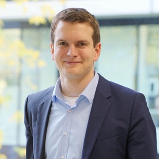 Dr. Titus Brinker, KI-Experte, lacht in die Kamera. Er verrät, wie Künstliche Intelligenz die Medizin verändert.