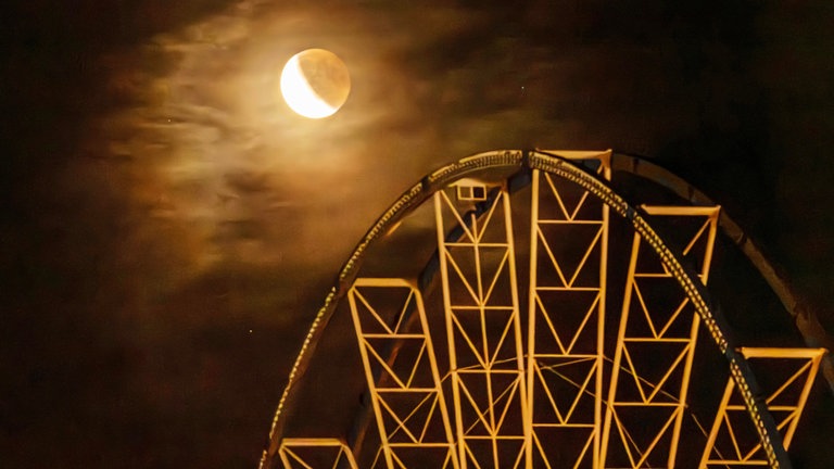 8. September: Die Mondfinsternis begeisterte viele Menschen in Deutschland. Hier zeigt sich der Himmelskörper über dem Riesenrad auf dem Münchner Oktoberfest, das in knapp zwei Wochen startet. Als er wieder sichtbar ist, leuchtet der rötliche "Blutmond" über dem nächtlichen Wiesnhimmel.