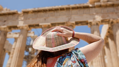Eine Frau mit Sonnenhut steht vor der Akropolis | Kuriose Regeln in Urlaubsländern