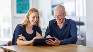 Eine Frau und ein Mann sitzen zusammen an einem Tisch mit einem Tablet | Warum Passwörter nicht geteilt werden sollten