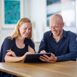 Eine Frau und ein Mann sitzen zusammen an einem Tisch mit einem Tablet | Warum Passwörter nicht geteilt werden sollten