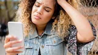 Eine junge Frau schaut frustiert auf ihr Smartphone | Fexting: Warum wir uns über Textnachrichten schneller streiten