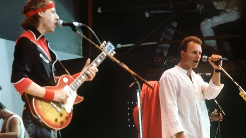 Mark Knopfler von der britischen Band "Dire Straits" (links) und der britische Rocksänger Sting von der Gruppe "Police" (retchts) bei ihrem gemeinsamen Auftritt während des Live Aid-Konzertes zugunsten der Hungerhilfe in Afrika im Wembley-Stadion in London. Beim Dire-Straits-Song "Money For Nothing" ist Sting als Gastsänger zu hören.