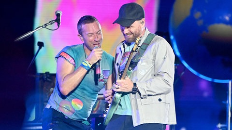 Man merkt ihnen den Spaß und die Freundschaft regelrecht an: Sänger Chris Martin und Gitarrist Jonny Buckland von Coldplay live auf der Bühne am 15.08.2024 im Olympiastadion in München, bei dem auch Songs ihres Debütalbums "Parachutes" mit auf der Setliste waren.