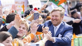 König William Alexander begrüßt beim Königstag in den Niederlanden die Menschen, die ihm zujubeln. Viele sind orange gekleidet. 