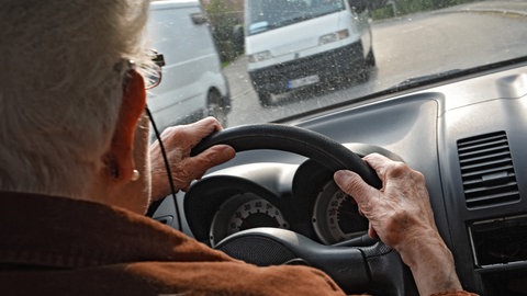 Seniorin am Steuer im Auto: Eine in die Jahre gekommene Frau mit weißem Haar lenkt das Fahrzeug.