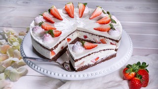 Die leckere Erdbeer-Schoko-Torte ist, wie im Rezept beschrieben, hergestellt worden und steht angeschnitten auf einer Kaffeetafel.